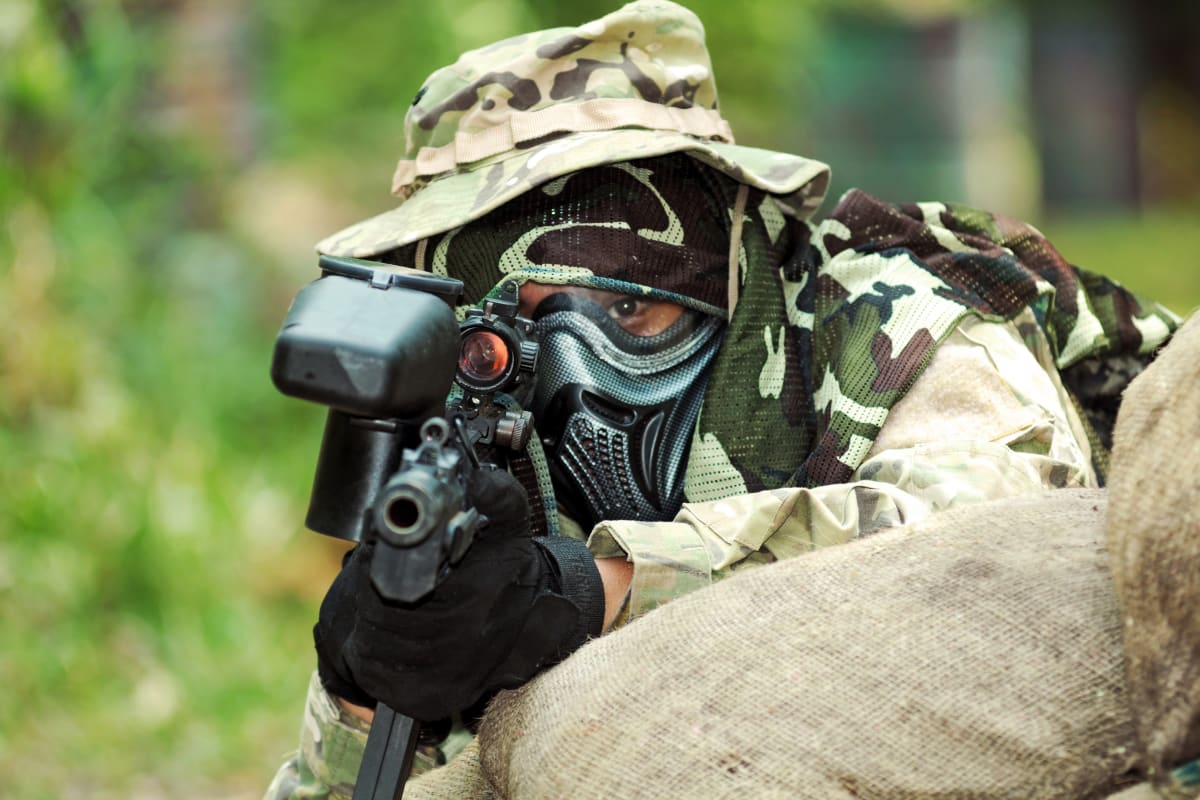 A man hides behind a sack during a game of paintball