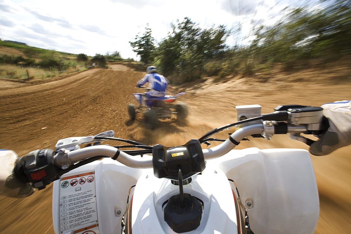 Two men racing quad bikes around a dirt track