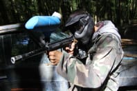 A man hides behind a 4x4 vehicle during a game of paintball