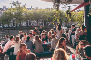 Waterkant Amsterdam during busy day time people enjoying drinks