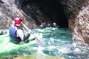 a group of guys paddle through cave in a kayak
