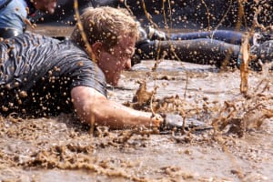 A man crawling through mud on assault course