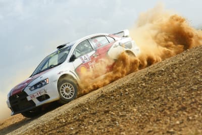 A rally car speeds around a dirt road