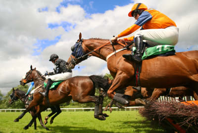 Horses racing and jumping over a fence