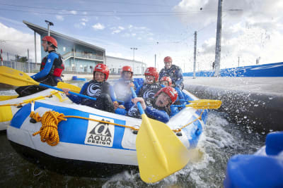 A laughing group paddle down rapids on a man made rafting course